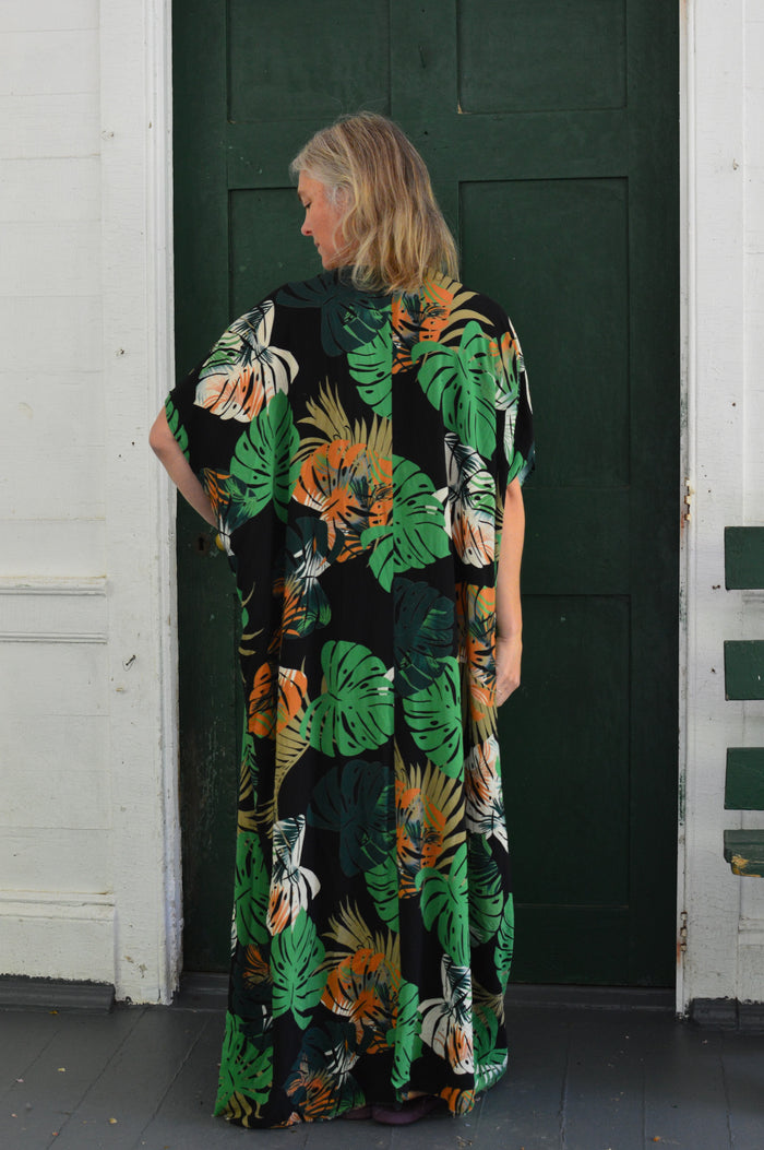Back of white woman wearing a tropical green and orange print kaftan standing in front of a green door.