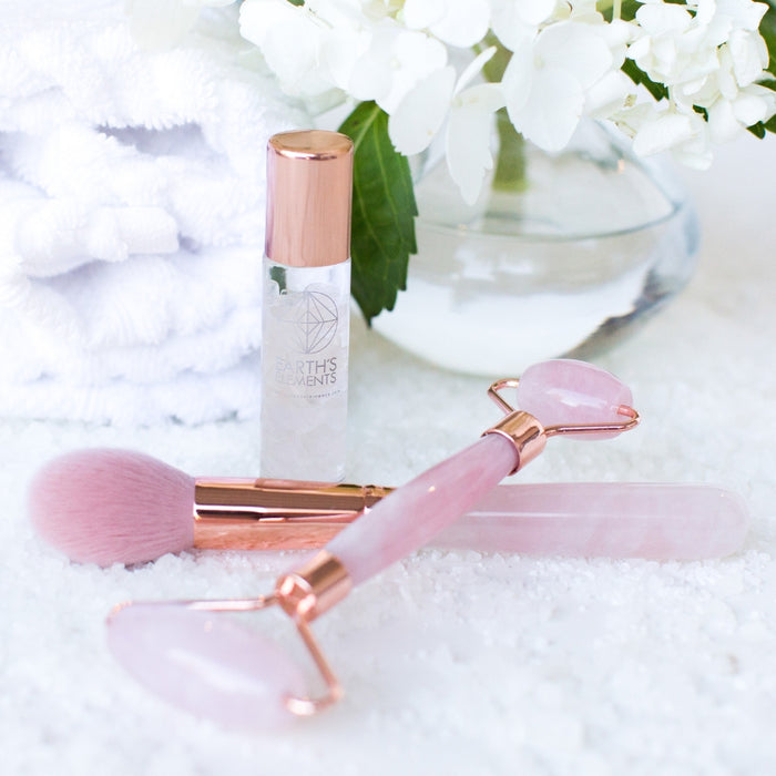 Beauty tools including a roller and brush on a white surface with flowers in the background
