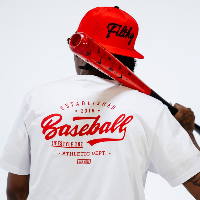 Person wearing a white t-shirt with 'Baseball Lifestyle 101' text and a red cap holding a red bat
