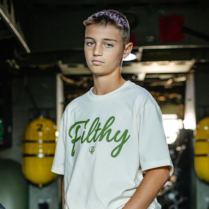 Youth Beige T-shirt with olive green ‘Filthy’ lettering and BL101 logo across chest on person.