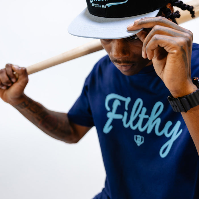 Person wearing a blue 'Filthy' t-shirt and black cap with a white rim, holding a baseball bat.