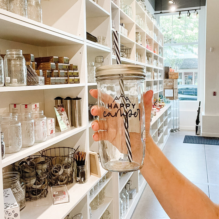 Mason jar tumbler that says “happy camper” with three mountain peaks above