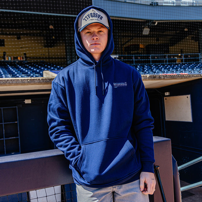 Person wearing a blue hoodie and cap standing in an empty stadium.