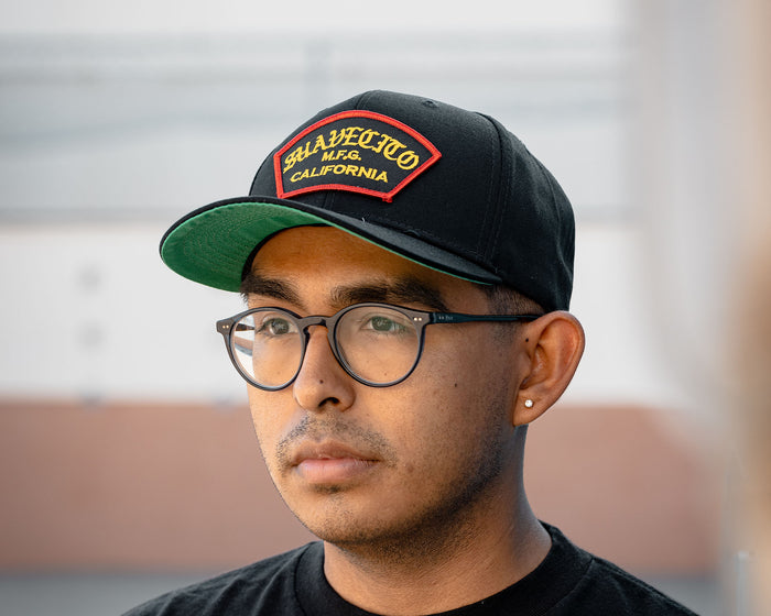 man wearing - suavecito hat with yellow embroidered text and red border outline "suavecito m.f.g. california"