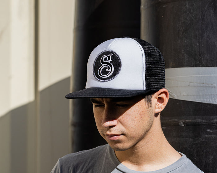 man wearing - suavecito hat with white embroidered text and black background with suavecito "S"
