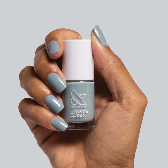 Quick Dry Mani System showing hand with muted blue-gray polish holding matching quick dry nail polish bottle