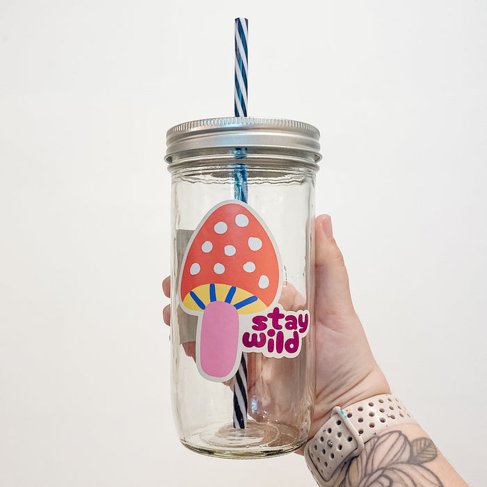 Hand holding a mason jar that reads stay wild with a colourful mushroom.