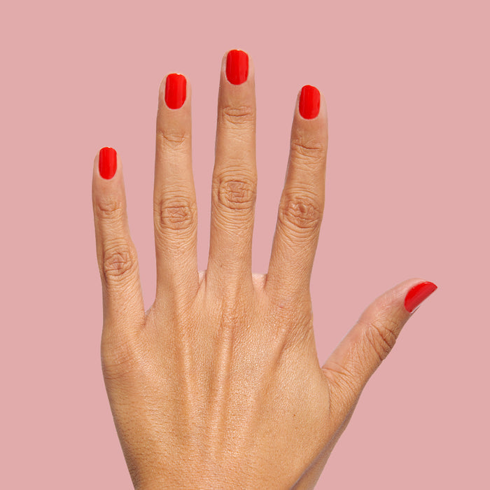 The Bold Mama Set showing hand with bright red-orange polish on neatly shaped nails against a soft pink background