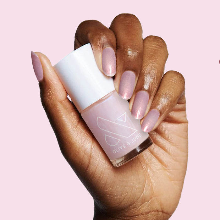 Hand with soft mauve polish holding Olive and June nail polish bottle from The Classic Mama Set for easy at-home mani.