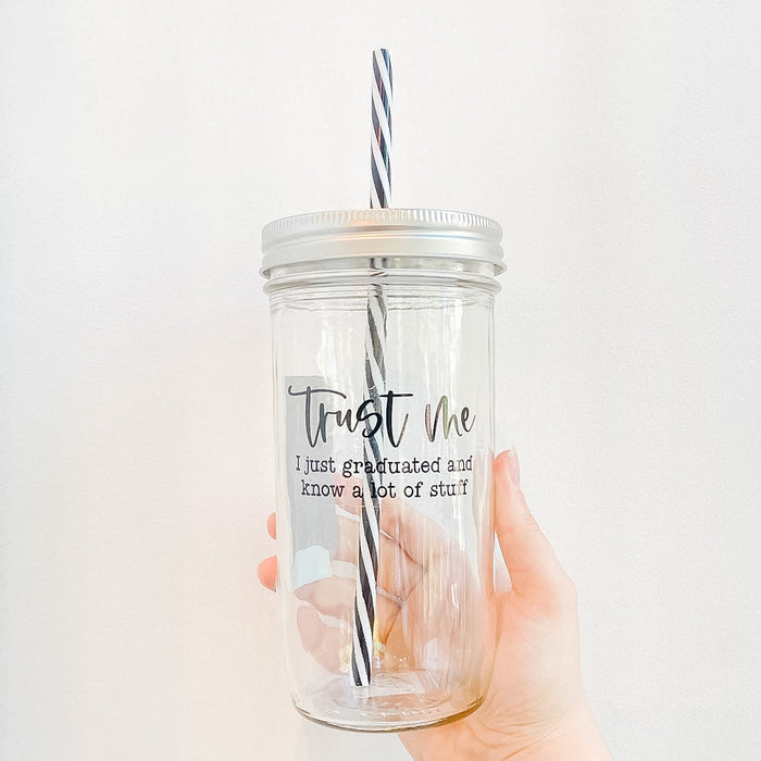 Glass mason jar tumbler with “Trust Me, I Just Graduated and Know a Lot of Stuff” design, reusable striped straw, and patterned mason jar style lid.