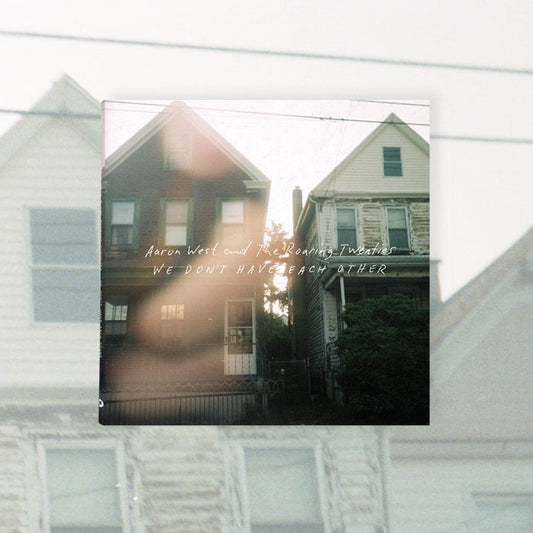 CD Album Cover for Aaron West and the Roaring Twenties 'We Don't Have Each Other'. Album cover shows two houses side by side with Aaron West and the Roaring Twenties 'We Don't Have Each Other' in white text over them.