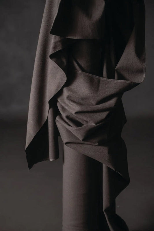 Cotton canvas fabric is a warm charcoal color. draped over a cylindrical object against a dark background.