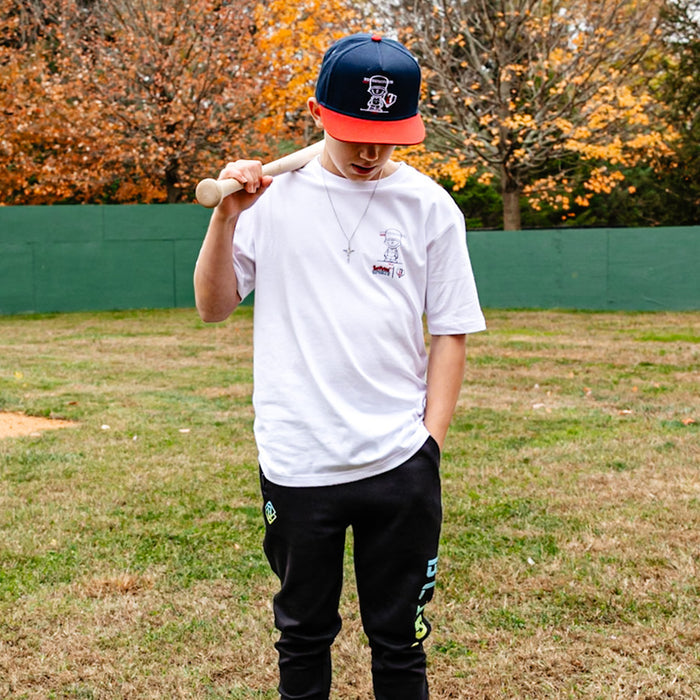 Person holding a baseball bat wearing whit Pablo Sanchez t-shirt in a grassy field with trees in the background