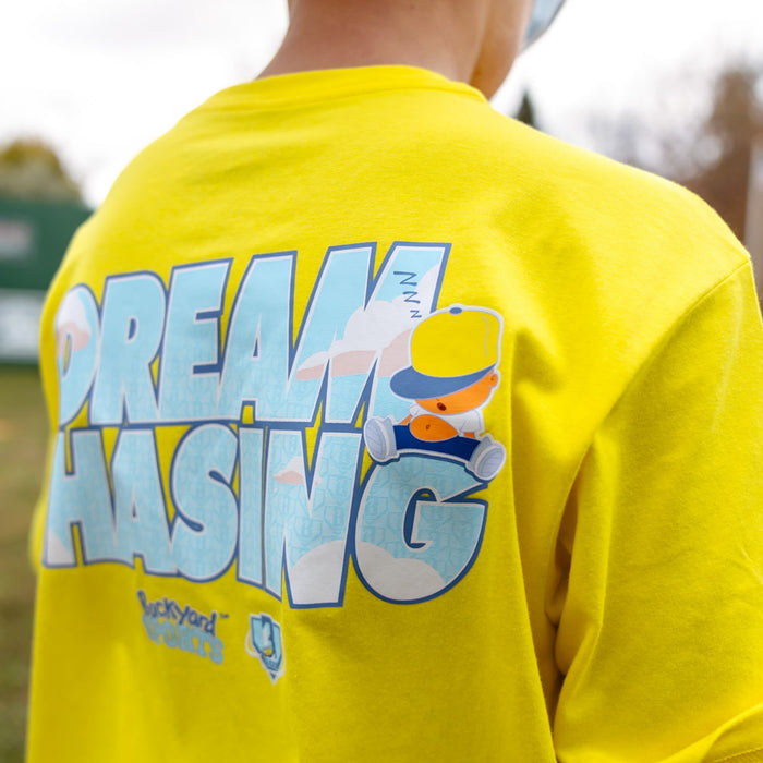 Yellow t-shirt with 'Dream Chasing' graphic and Pablo Sanchez cartoon on a blurred outdoor background