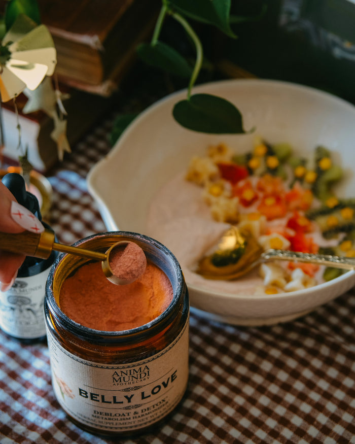 Jar of 'Belly Love' with a spoonful being taken, placed on a checkered tablecloth with a bowl of salad in the background.