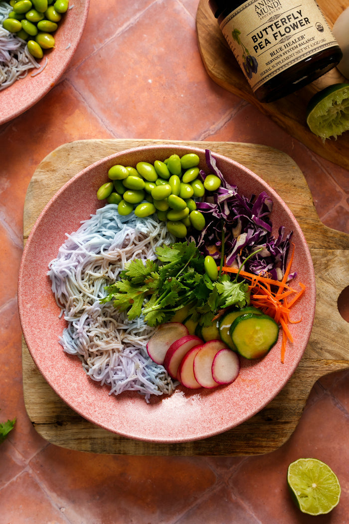 Pink plate with butterfly pea flower salad on a wooden cutting board