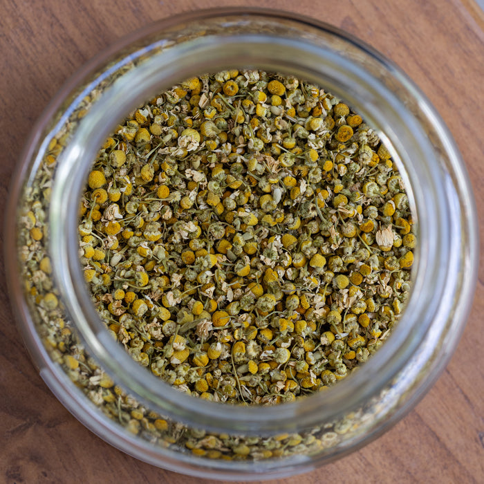 Glass jar filled with dried chamomile flowers on a wooden surface
