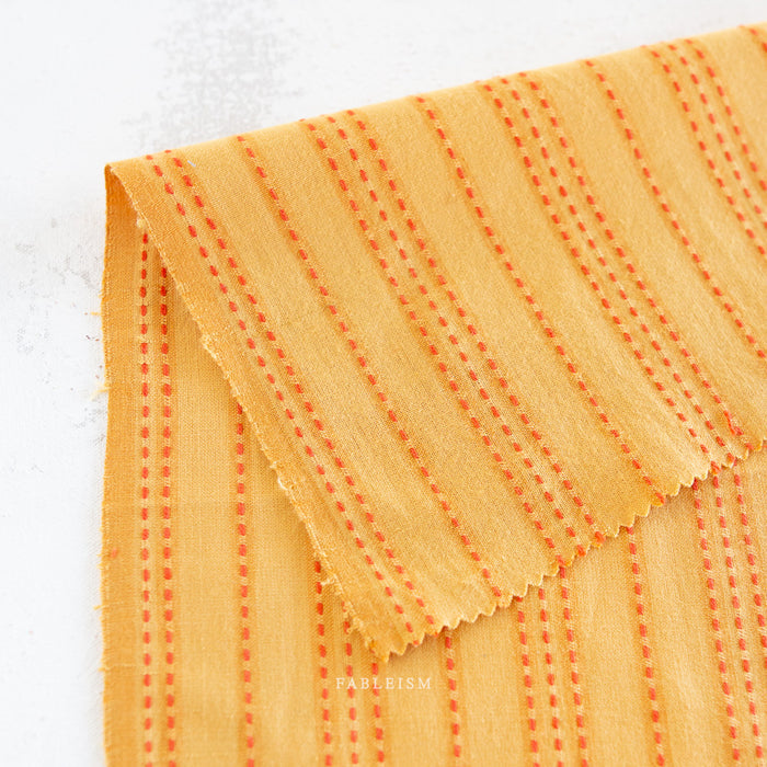 Close-up of orange fabric with red stitching on a white background