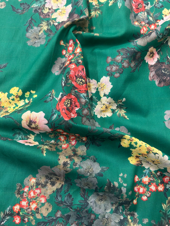 This is a cotton voile it has a vibrant and unsaturated floral print with yellow, pink and red flowers on a green background.