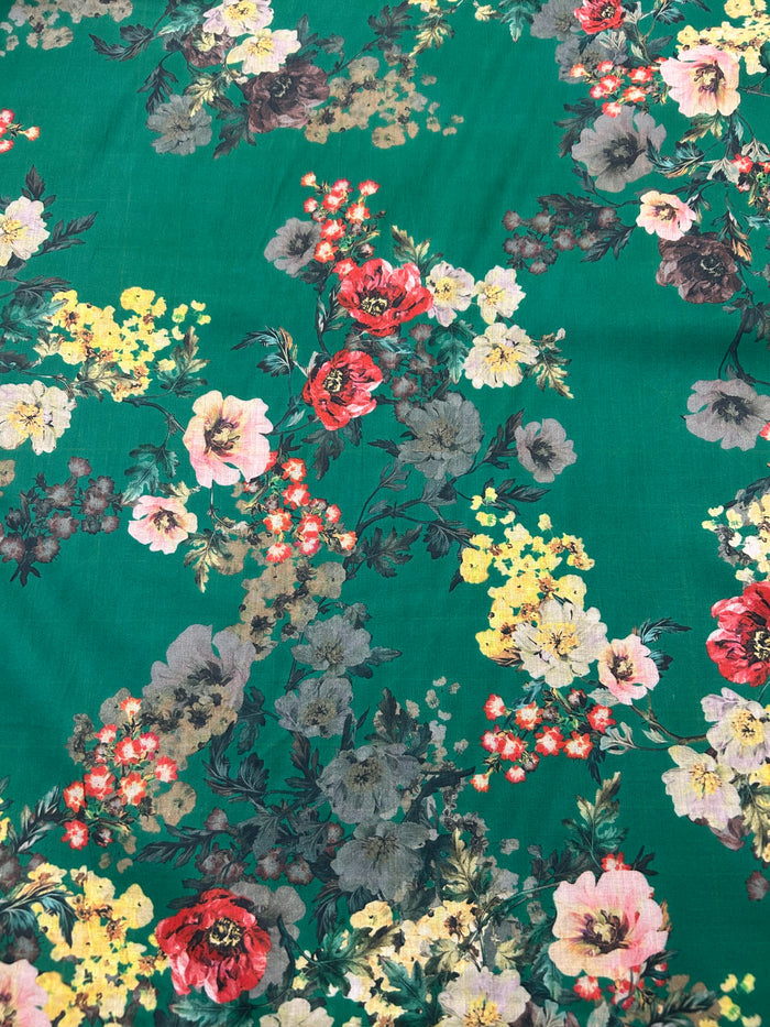 This is a cotton voile it has a vibrant and unsaturated floral print with yellow, pink and red flowers on a green background.