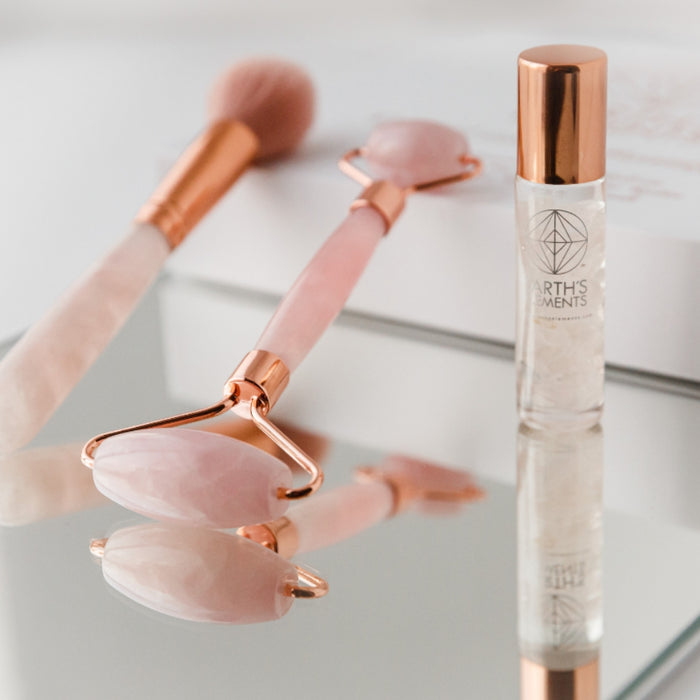 Rose gold facial roller and bottle of Skinesis Elements on a light background