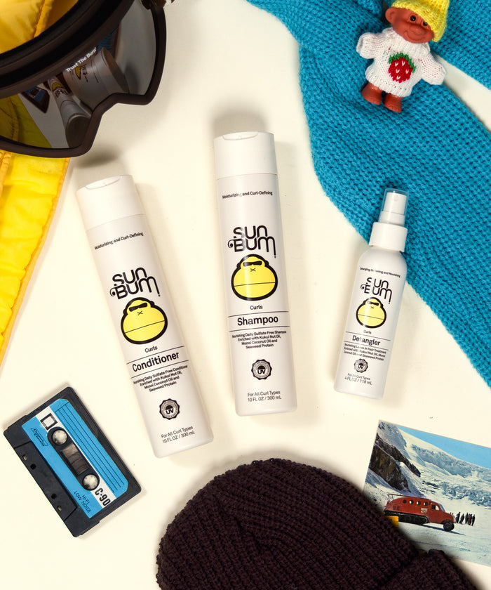 Sun Bum Curls Hair Care Bundle with shampoo, conditioner, and detangler surrounded by winter accessories and retro items