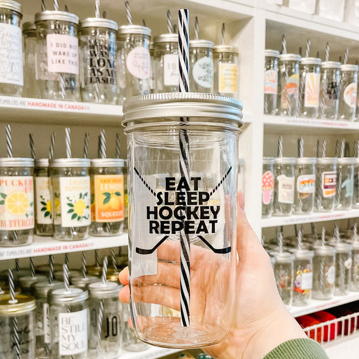 Hand holding mason jar tumbler that reads eat sleep hockey repeat in black ink on clear background
