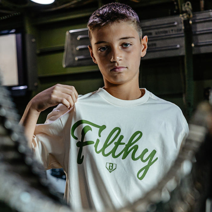 Youth Beige T-shirt with olive green ‘Filthy’ lettering and BL101 logo across chest on person.