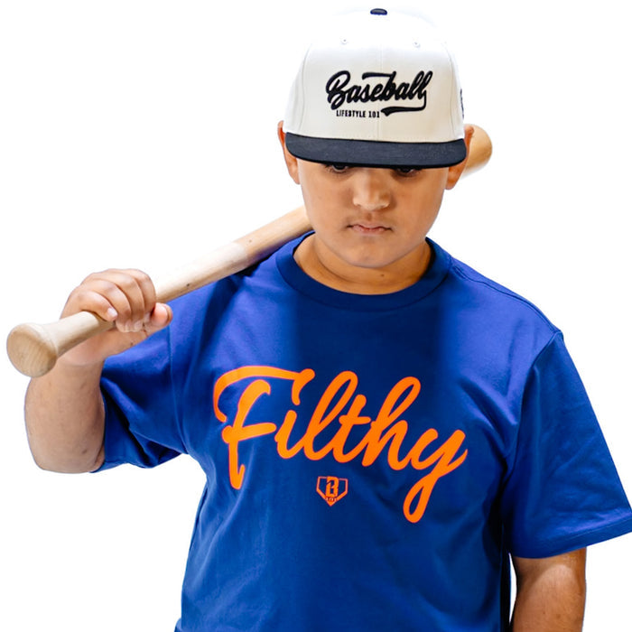 Child wearing a blue t- shirt with orange 'Filthy' text and white baseball cap with BL101 logo, holding a wooden bat.