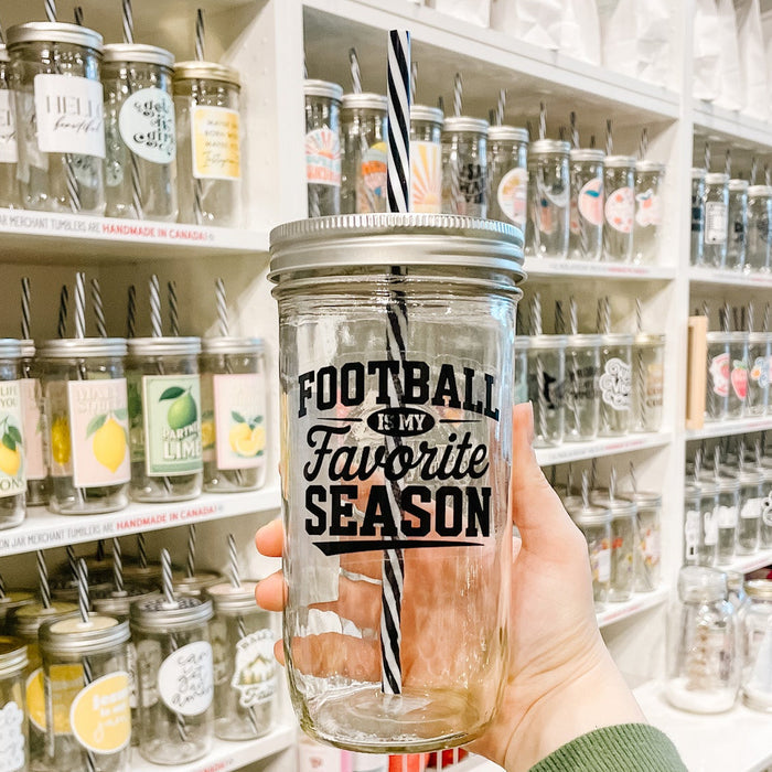Hand holding a mason jar tumbler that reads football is my favorite season in black ink on clear background