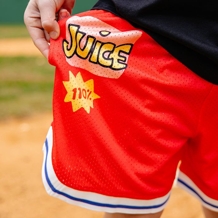 Red shorts with 'Juice' and '110%' text held by a person on a grassy field.