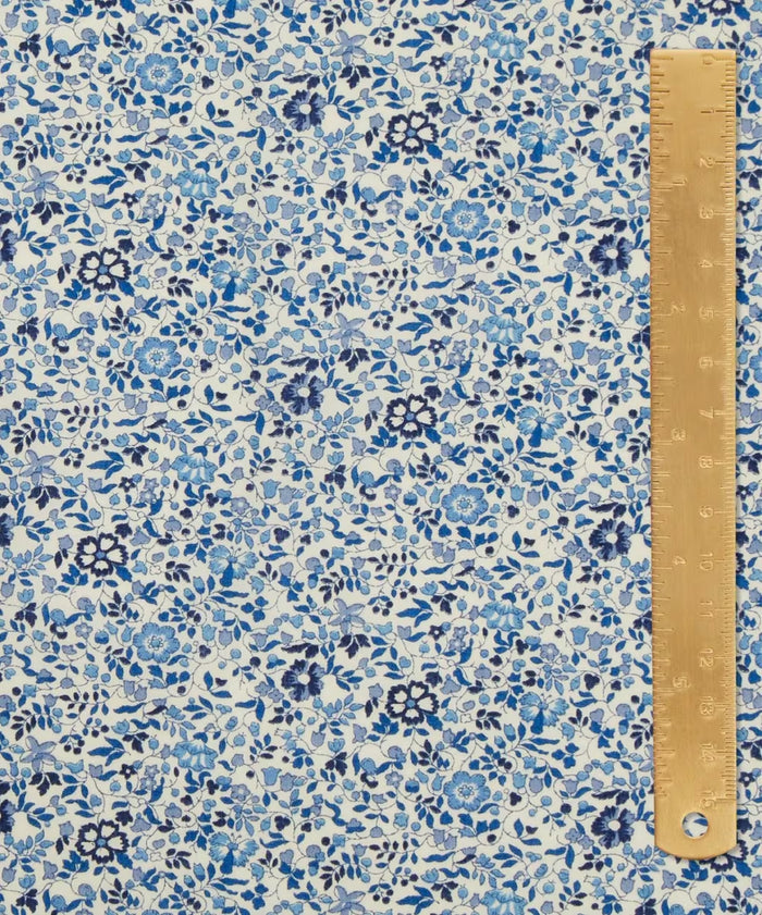 Close up of a cotton in a ditsy floral print with dainty blue flowers with a white background. A light brown ruler on top.