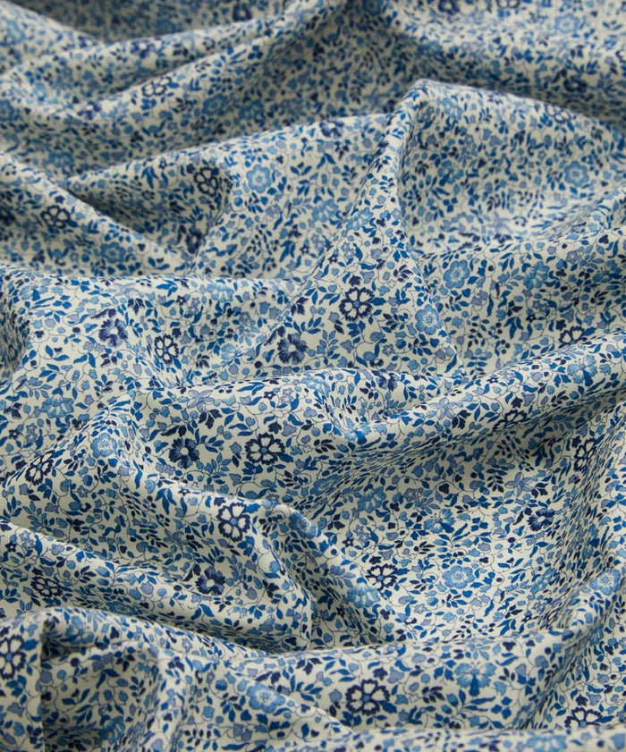A close up of cotton fabric in a ditsy floral print with dainty blue flowers with a white background.
