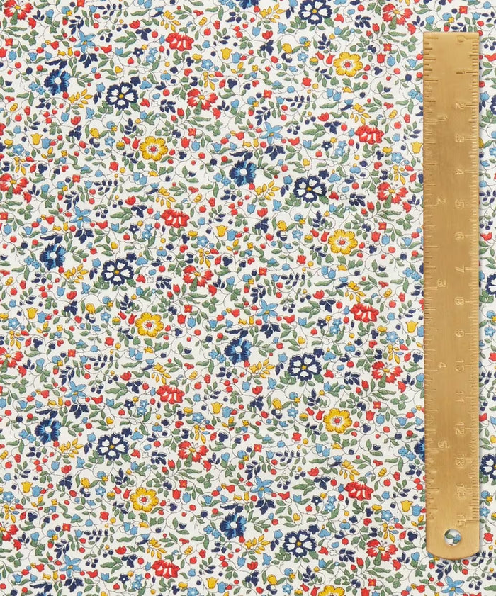 Close up of fabric with a beautiful vintage ditsy floral print of blue, reds, greens, and yellows. And a light brown ruler on top