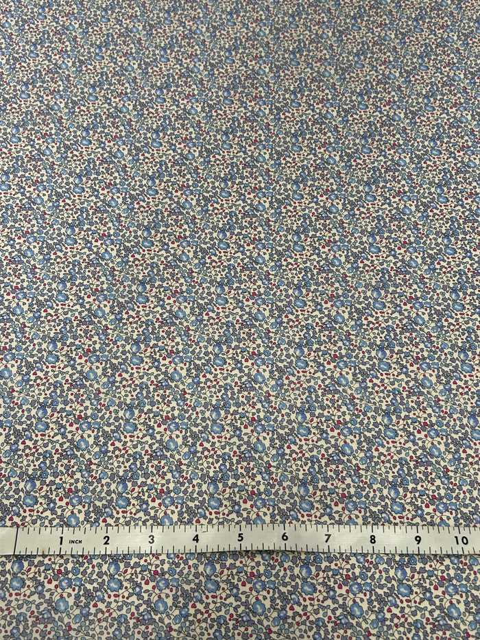 vintage ditsy floral cotton print with dainty blue round flowers with red buds on a white background with a white measuring tape.