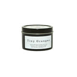 Small orange candle in a Little Cow Co. tin with a cute cow illustration, ideal for cozy home decor.
