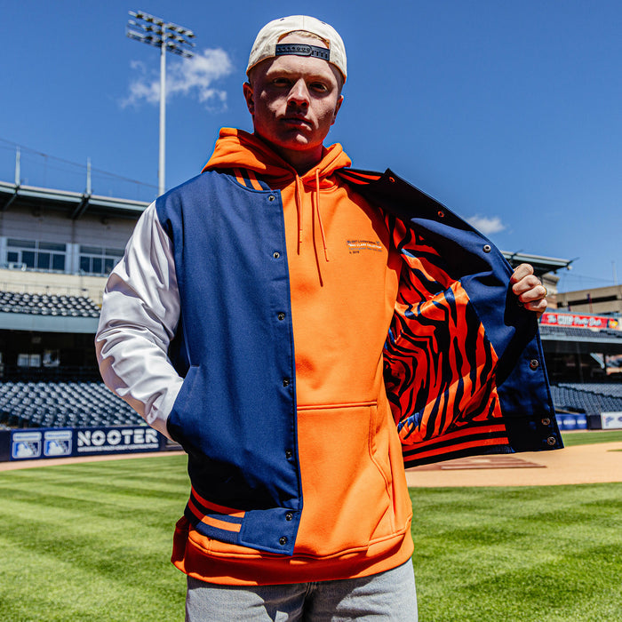 Person wearing a blue and orange jacket with a tiger design on a baseball field