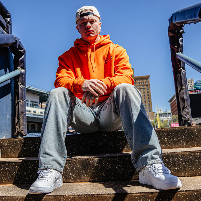 Person wearing an orange hoodie and light blue jeans sitting on steps with a cityscape background