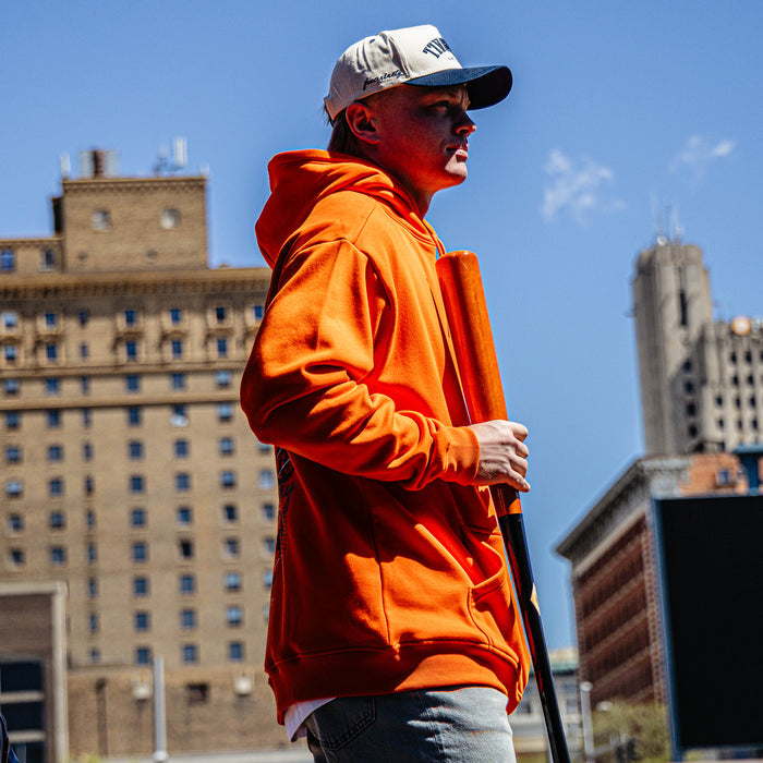 Person wearing an orange hoodie and cap with a cityscape background