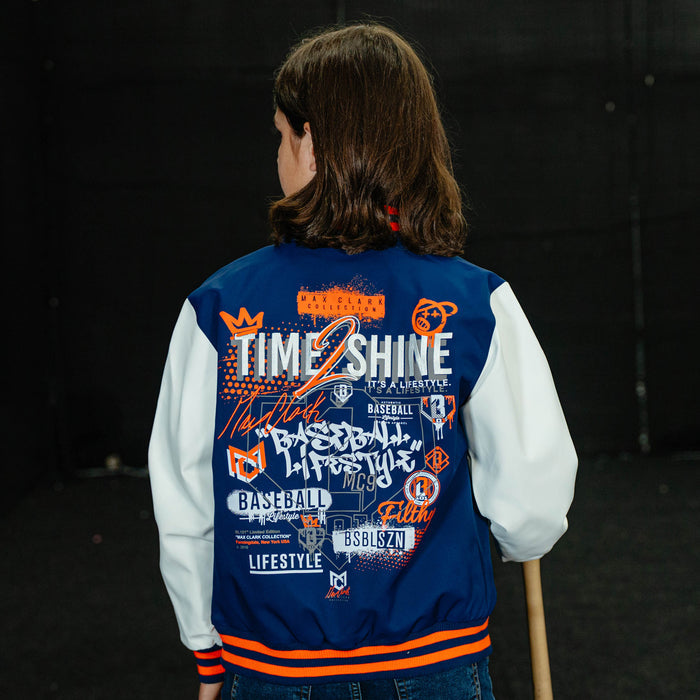 Person wearing a blue and white varsity jacket with text and graphics, standing against a dark background.