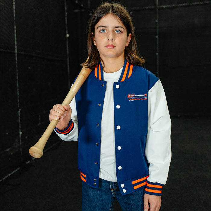 Person wearing a blue and white letterman jacket with orange accents, holding a baseball bat against a black background.