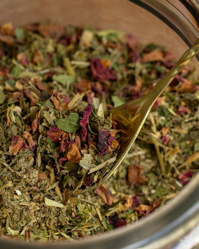 Herbal tea mix in a glass jar with a gold spoon