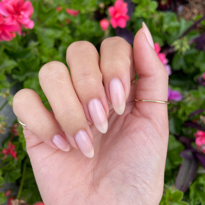 Hand with natural almond-shaped nails featuring a soft translucent pink mani using Mother of Pearl polish outdoors