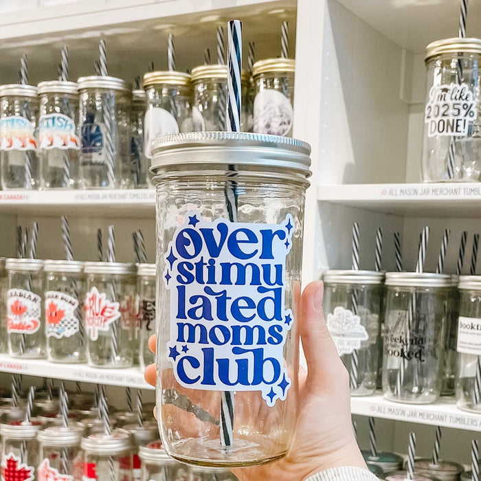 Hand holding a mason jar tumbler that reads overstimulated moms club in dark and light purple