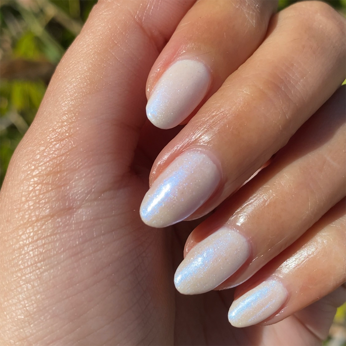 Hand with soft iridescent pale pink nails showing a glossy manicure from the Pink Opal Set by Olive and June
