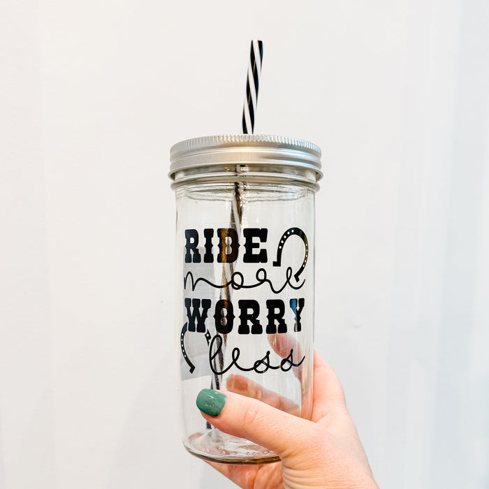 Hand holding mason jar tumbler that says ride more worry less in black in on clear design