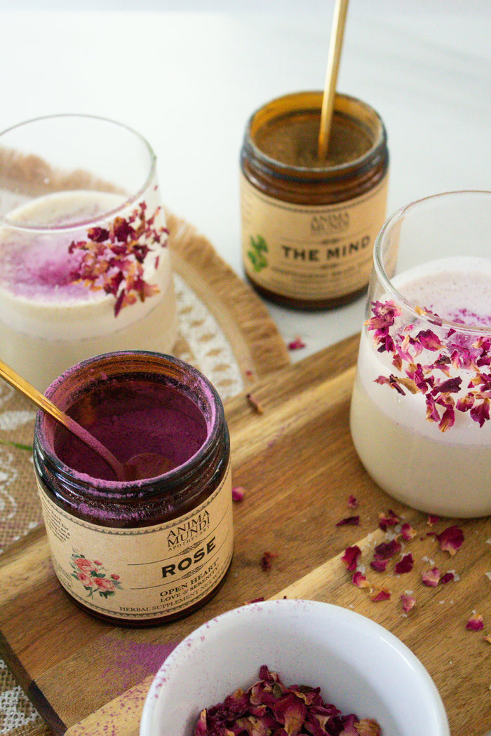 Jars of rose and other scented products with glasses of a creamy beverage on a wooden tray.