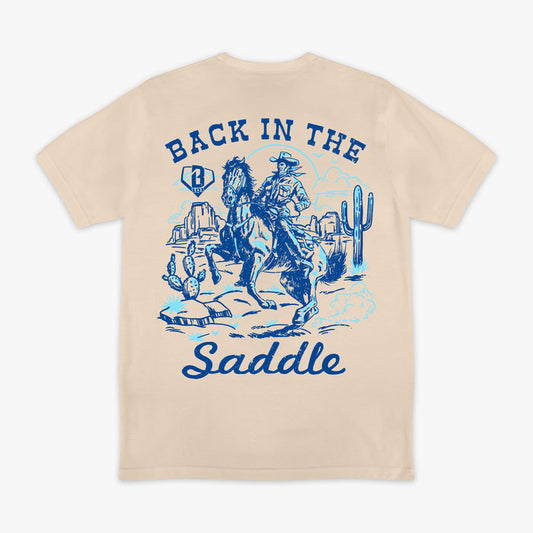 Beige t-shirt with blue graphic of a cowboy and text 'Back in the Saddle' on a white background