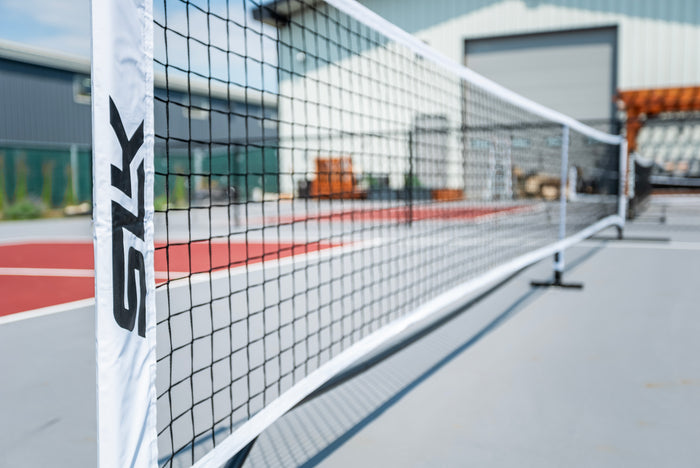 Close-up of a court net and white post with SZK logo on an outdoor pickleball/tennis court.