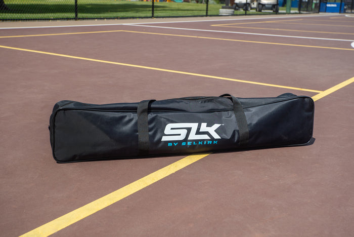 Black SLK BY SELKIRK soft paddle bag resting on painted outdoor pickleball court